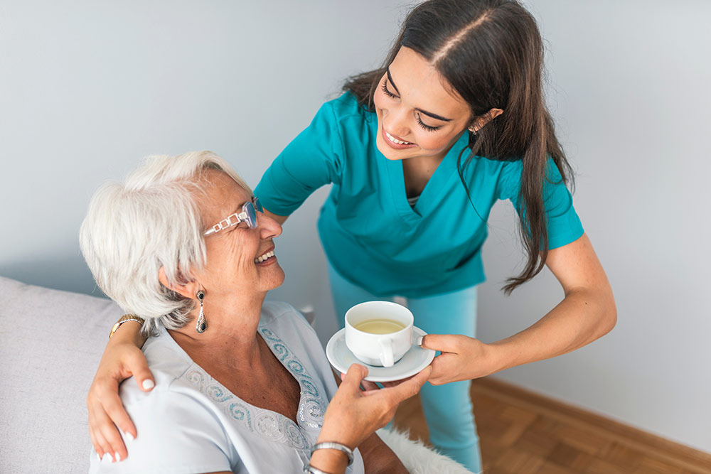 Senior woman with caregiver getting tea at dementia memory care community