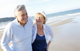 Senior couple walking along beach smiling and happy