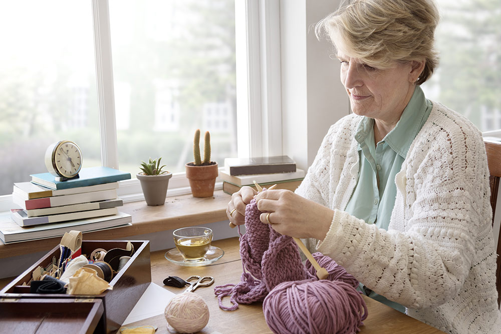 Senior woman sitting at table in assisted living apartment knitting
