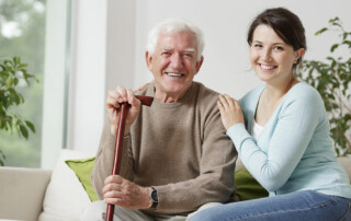 Senior man holding cane sitting on couch next to daughter
