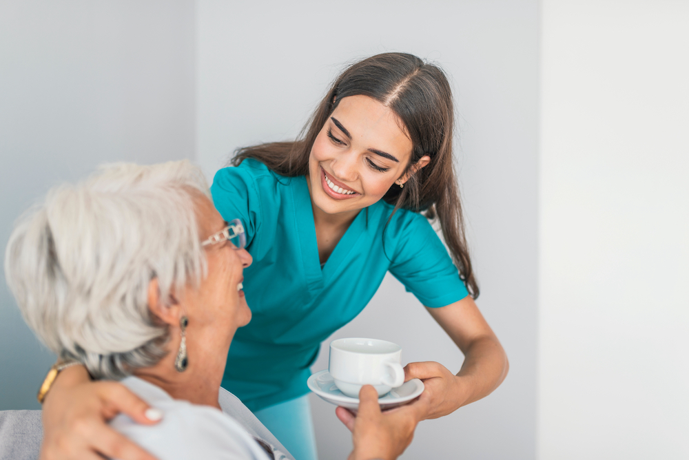 A caregiver giving a senior woman a cup of tea