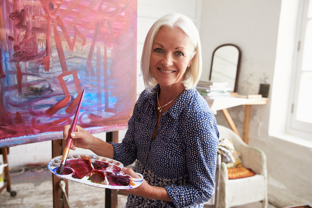 A senior woman paints on a large canvas