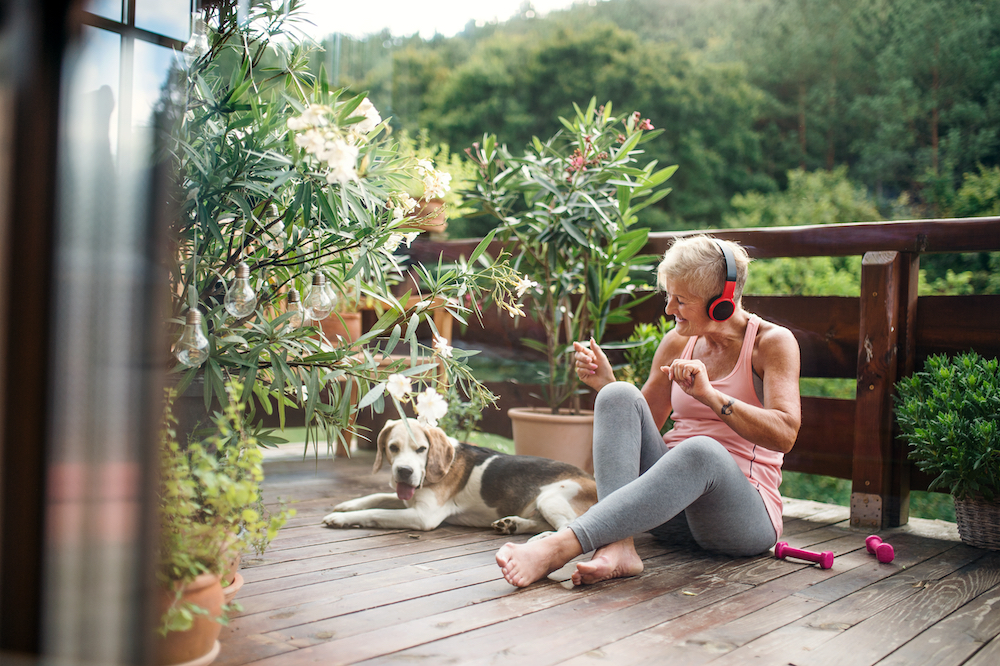 A senior woman sits outside with her dog and listens to music on her headphones