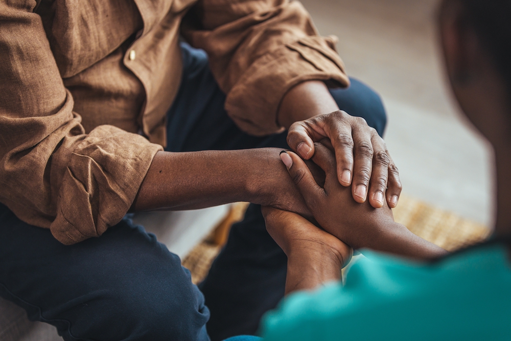 A senior man holds hands with his caregiver at memory care