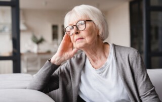 A senior woman wearing glasses looks out a window