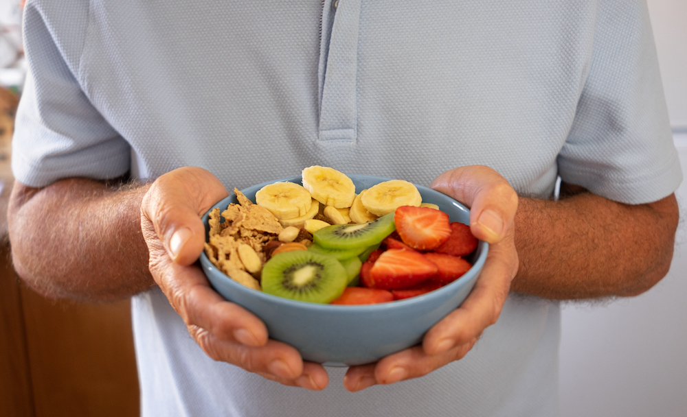 A senior man holding a bowl of fruits
